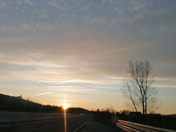 Road by silhouette trees against sky during sunset