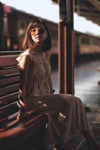 Young woman sitting on seat at railroad station platform