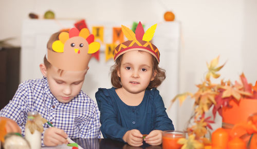 Portrait of girl wearing paper hat sitting with brother at home