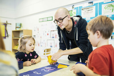 Male teacher assisting students in art class at kindergarten