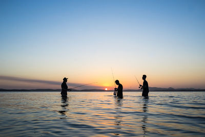 Silhouette men on sea against sky during sunset