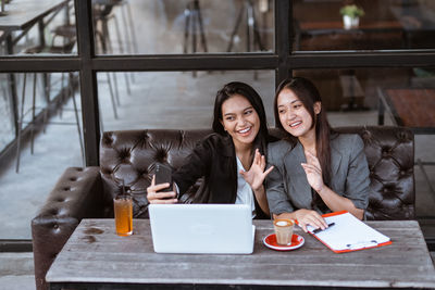 Portrait of smiling young woman using mobile phone while sitting in cafe