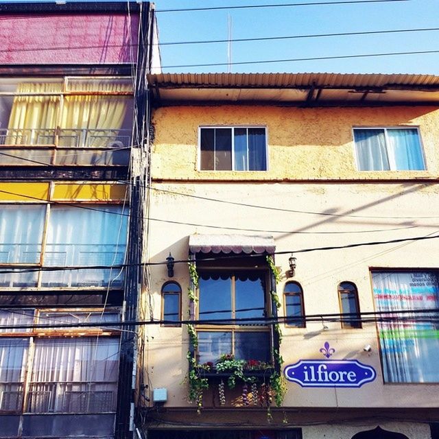 architecture, building exterior, built structure, window, low angle view, building, residential building, text, graffiti, residential structure, western script, city, day, outdoors, no people, blue, power line, balcony, house, yellow