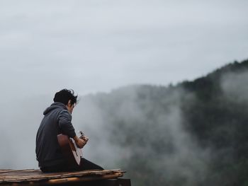 Man sitting on mountain against sky