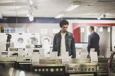 Contemplating young customer looking at appliances while standing in electronics store