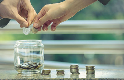 Cropped hands of people putting coins in jar on table