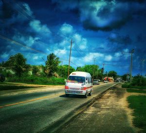 Cars on road against cloudy sky