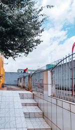 Fence by footpath against sky in city