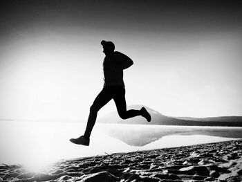 Silhouette man jumping in sea against sky