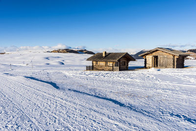 Houses on snow covered land by buildings against blue sky