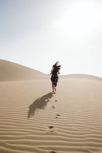 Back view of young woman running on sand dune between desert and blue heaven in evening in canary islands, spain