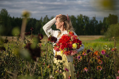 A cute girl in a sweater stands in an autumn field with flowers