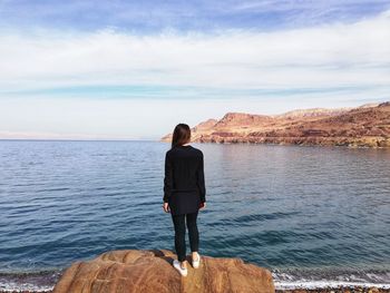 Rear view of woman standing on rock at sea against sky