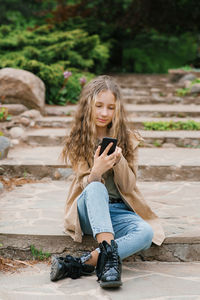 Teenage girl communicates online in a smartphone, sitting in nature in the spring in the park person