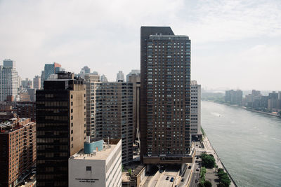 Modern buildings by river in city against sky