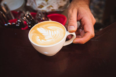 Cropped hand of barista holding coffee cup on table at cafe