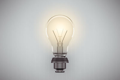 Close-up of illuminated light bulb against white wall