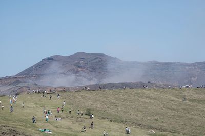 People on field by mountains against clear sky