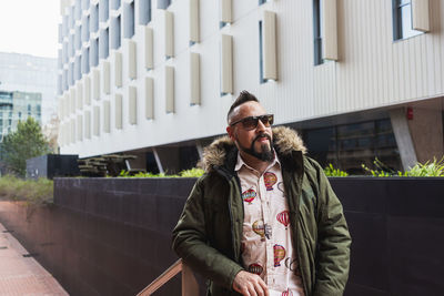 Bearded man standing and relaxing on stairs against office building