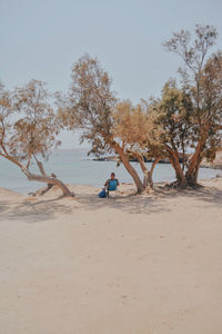 Man sitting on sand at beach against sky