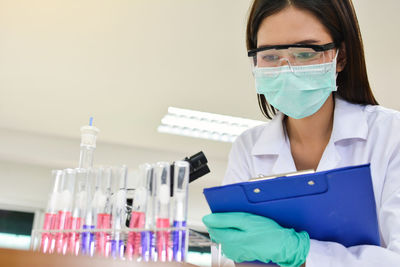 Female scientist with clipboard looking at test tubes in laboratory