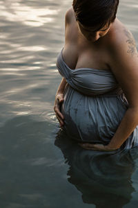 Midsection of pregnant woman standing by lake