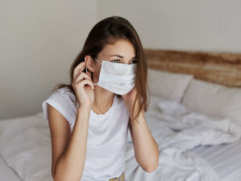 Woman wearing mask while sitting on bed at home