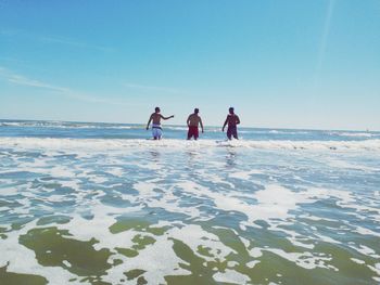 Rear view of men on beach against clear sky