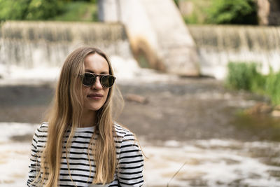 Portrait of a woman in a striped top and sunglasses in front of the dam by the river