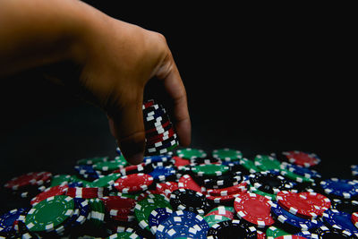 Cropped hand spilling gambling chips on black background