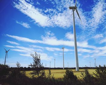 Low angle view of wind turbines on field against sky