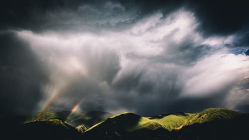 Scenic view of rainbow over mountains against cloudy sky