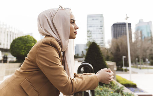 Young woman wearing hijab leaning on railing at office park