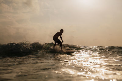 Silhouette man surfing in sea against sky