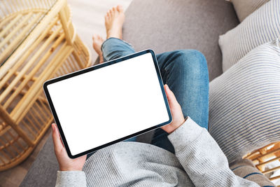 A woman holding black tablet pc with blank desktop white screen while lying on a sofa at home