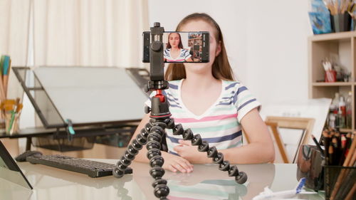 Woman photographing while sitting on table at home