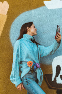 Midsection of woman using mobile phone against wall