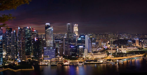 Illuminated buildings by river against sky at night