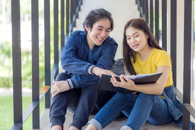 In the university campus, two asian couples sit on the stairwell with their thumbs up, working