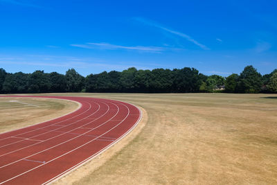 Empty athletics running track amidst field and trees on horizon against blue sky with copy space 