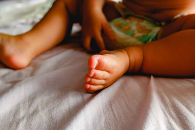 Low section of baby relaxing on bed