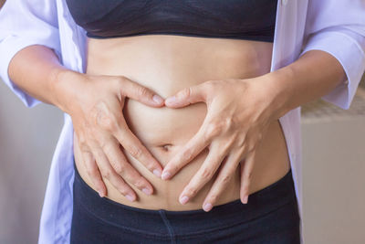 Midsection of pregnant woman making heart shape on stomach 