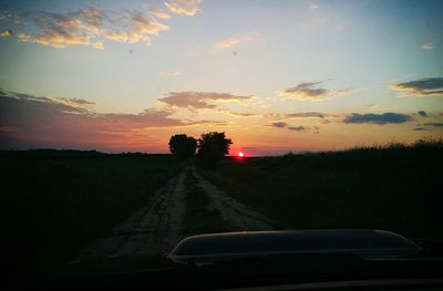 Road passing through field at sunset