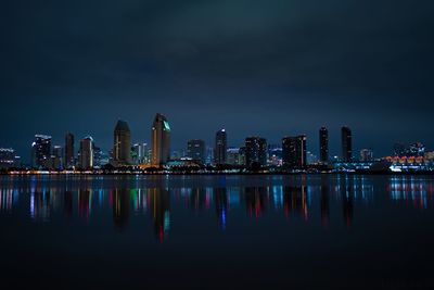 Illuminated buildings by river against sky at night