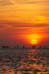 Silhouette people on beach against orange sky