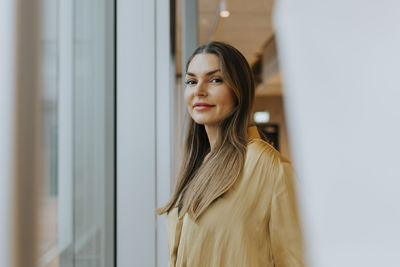 Portrait of smiling businesswoman standing near window at office