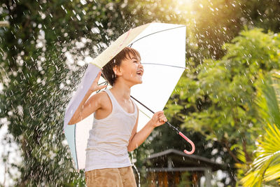 Woman holding umbrella while standing by tree during rainy season