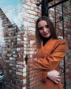 Portrait of young woman standing against brick wall