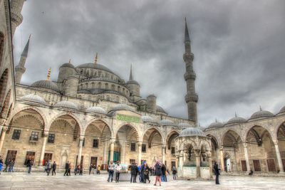 Tourists in front of building against cloudy sky