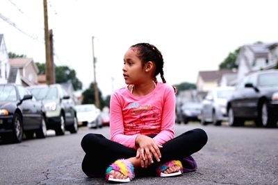Full length of teenage girl sitting on street in city